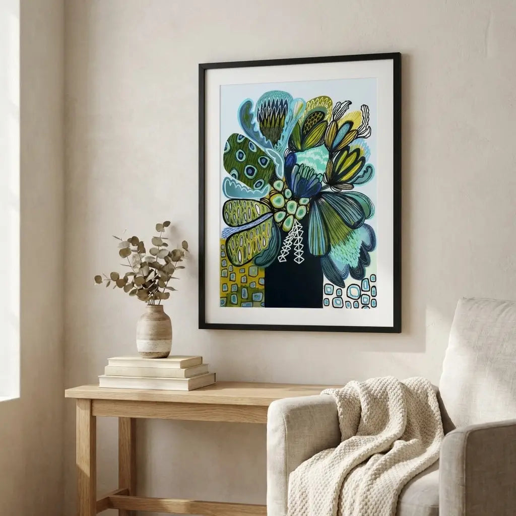 Framed abstract artwork on a wall above a wooden side table with a vase and books.
