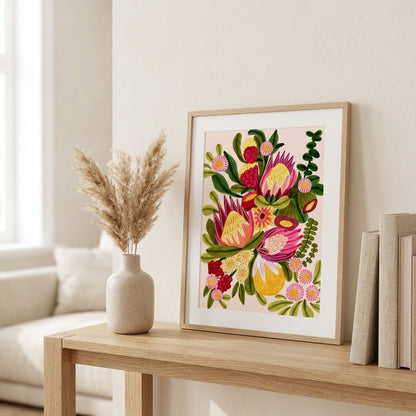 Framed floral artwork on a table with a vase and books in a bright room.