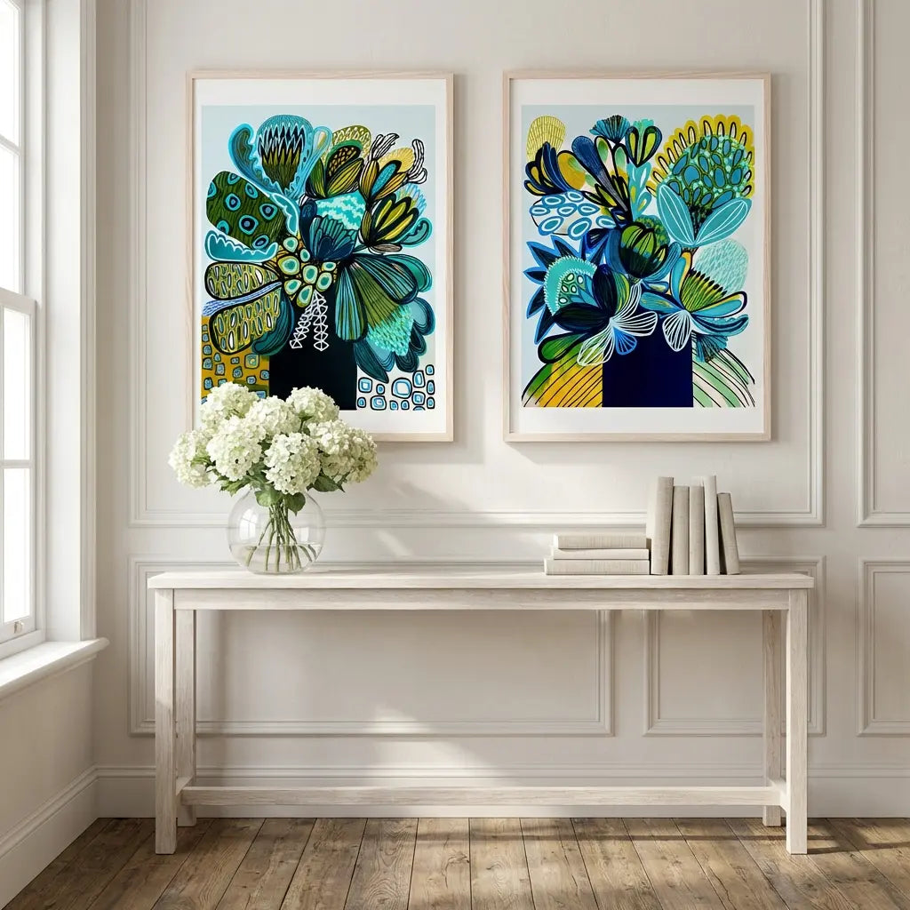 Two modern abstract artworks on a wall above a table with a vase of flowers and books.