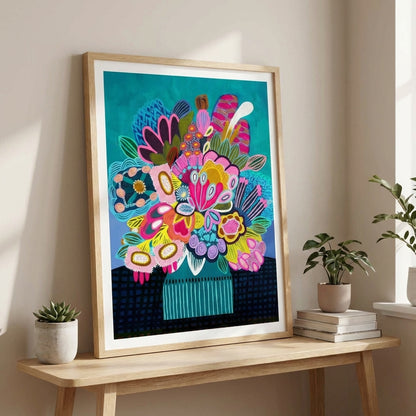 Colorful abstract floral artwork in a wooden frame on a table with plants and books.
