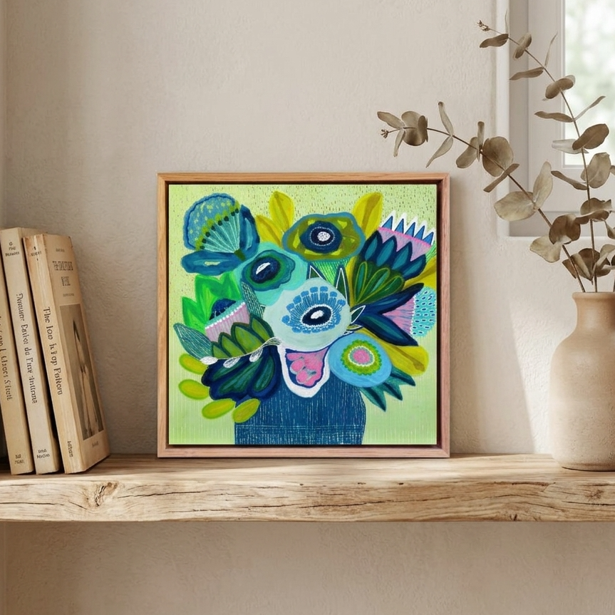 A colorful framed abstract painting featuring a stylized face with blue, green, yellow, and pink details, displayed on a wooden shelf next to books and a vase with dried branches.