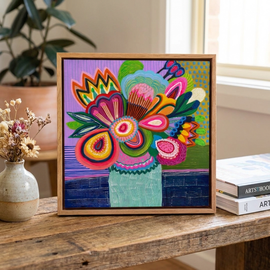 Colorful floral artwork in a wooden frame on a table with books and a vase.