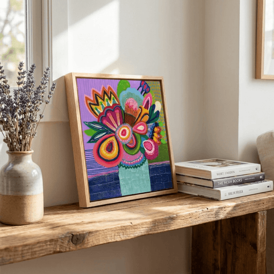 Colorful abstract artwork in a wooden frame on a wooden surface with books and a vase.