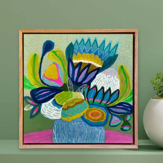 Framed colorful floral painting by Kirsten Katz on a green wall with decorative plants.