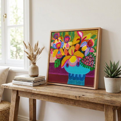 Colorful floral artwork in a wooden frame on a wooden table with books and plants.