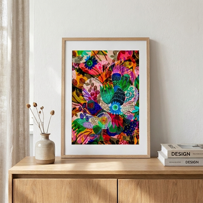Colorful abstract art print in a wooden frame on a wooden surface with books and a vase.