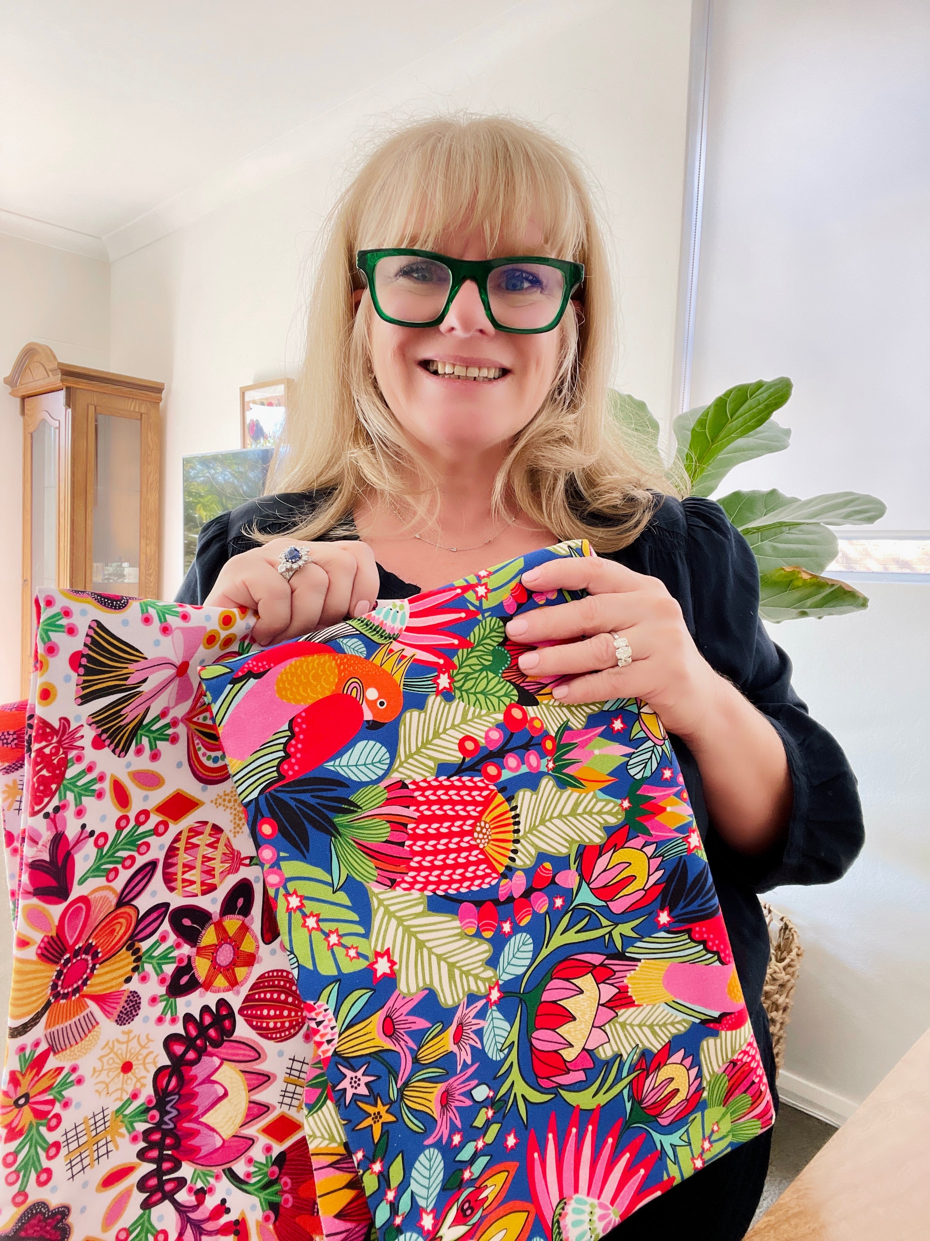 Kirsten Katz holding colorful fabric with floral and parrot pattern in a home setting