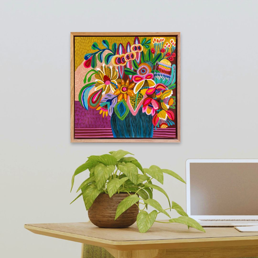 Colorful floral artwork on a wall above a desk with a plant and laptop.