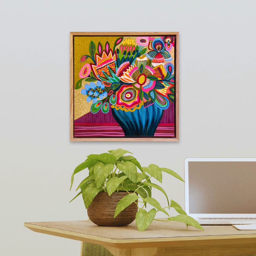 Colorful floral artwork on a wall above a desk with a plant and laptop.