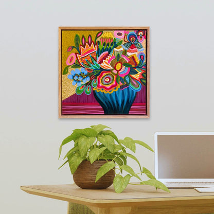 Colorful floral artwork on a wall above a desk with a plant and laptop.
