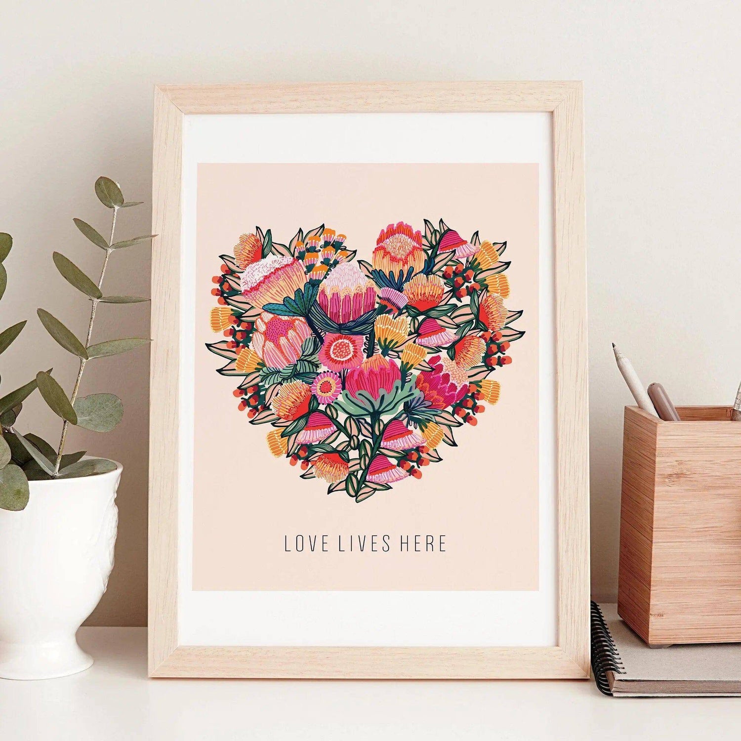 Love Lives Here Floral Heart art print by Kirsten Katz — proteas and gum blossoms arranged into a heart on soft peach